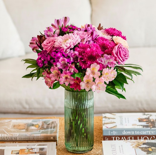 Vibrant mixed flower bouquet with pink roses, daisies, and alstroemeria in a glass vase.