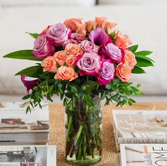 Vibrant floral bouquet featuring pink and purple roses with lush greenery in a glass vase.