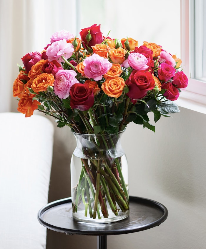 Vibrant bouquet of pink, orange, and red roses elegantly arranged in a clear vase.