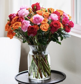 Vibrant floral arrangement with pink, orange, and red roses in a clear glass vase.