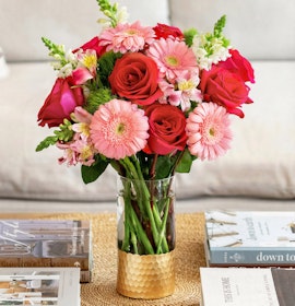 Colorful floral arrangement featuring pink gerbera daisies, red roses, and greenery in a vase.