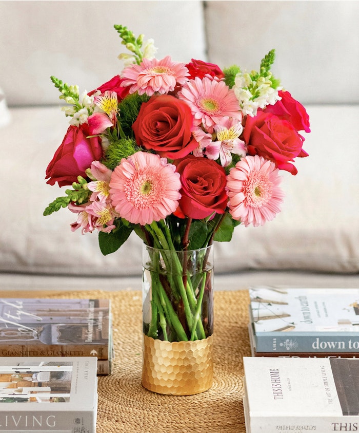 Colorful floral arrangement featuring pink gerbera daisies, red roses, and greenery in a vase.