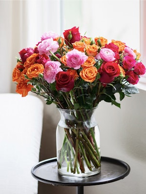 Vibrant bouquet of mixed roses in pink, orange, and red hues displayed in a glass vase.