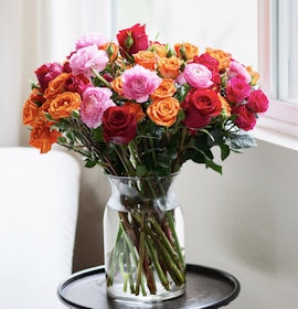 Vibrant bouquet of mixed roses in pink, orange, and red hues displayed in a glass vase.