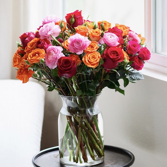 Vibrant bouquet of mixed roses in pink, orange, and red hues displayed in a glass vase.
