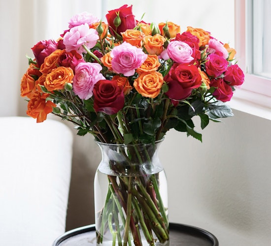 Vibrant bouquet of mixed roses in pink, orange, and red hues displayed in a glass vase.