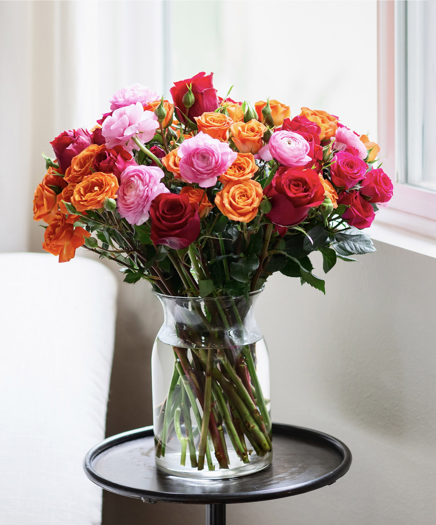 Vibrant bouquet of mixed roses in shades of pink, orange, and red arranged elegantly in a vase.
