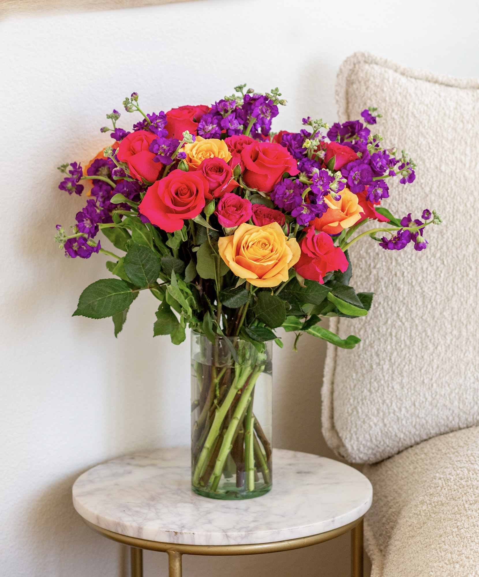 Vibrant mixed rose bouquet with orange, pink, and purple blooms in a chic glass vase.