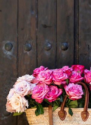 Charming woven basket filled with vibrant pink and soft beige roses, displayed against a rustic door.