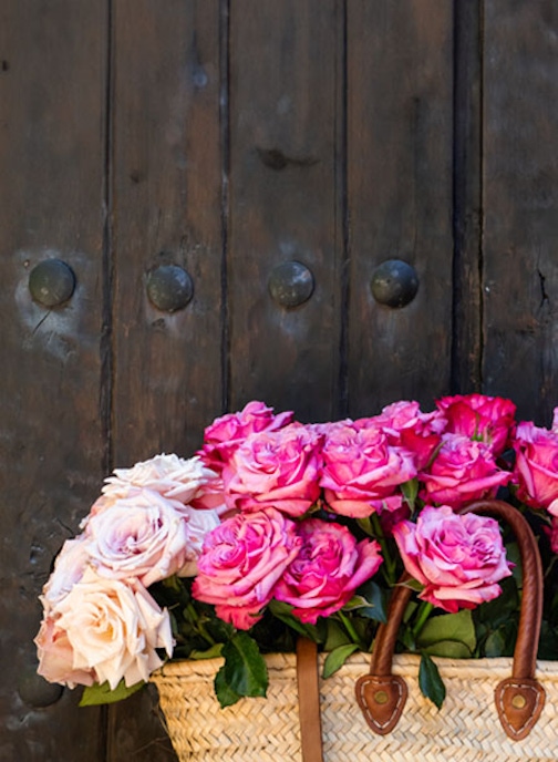 Charming woven basket filled with vibrant pink and soft beige roses, displayed against a rustic door.