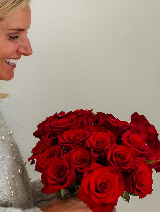 A woman joyfully holds a stunning bouquet of vibrant red roses, perfect for celebrations.