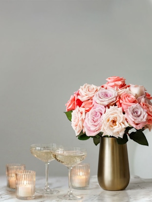 Elegant pink and white rose bouquet in a gold vase, complemented by sparkling cocktails and candles.