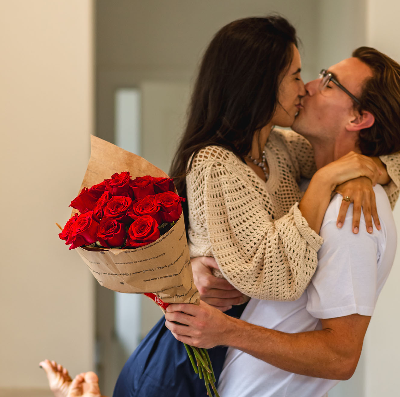 A joyful couple sharing a romantic kiss, holding a bouquet of vibrant red roses.