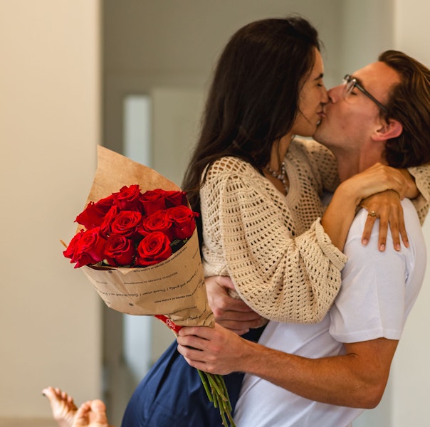 A joyful couple sharing a romantic kiss, holding a bouquet of vibrant red roses.
