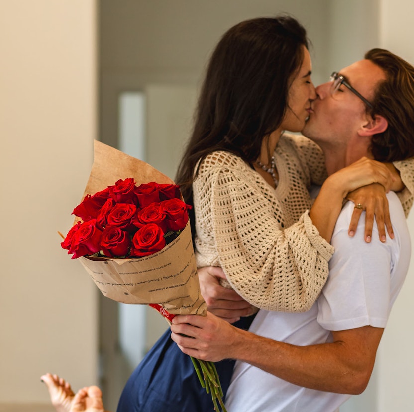 A joyful couple sharing a romantic kiss, holding a bouquet of vibrant red roses.