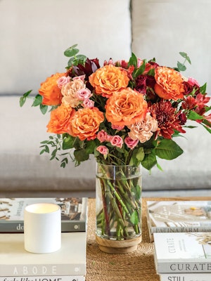 Vibrant orange and pink roses combined with lush greenery in a stylish vase.