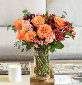 Vibrant orange and pink roses combined with lush greenery in a stylish vase.