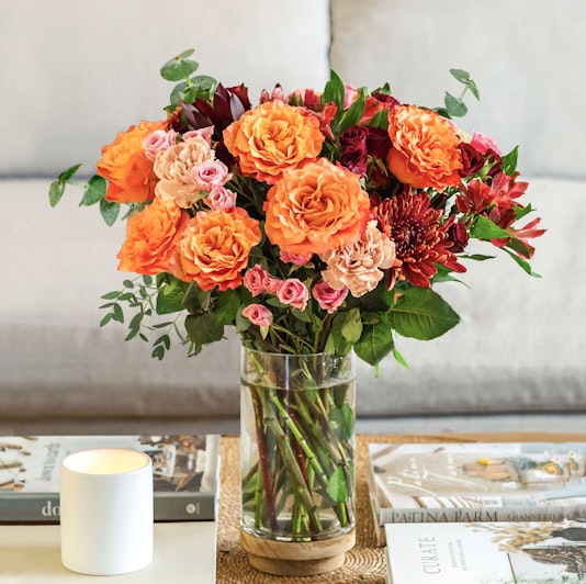 Vibrant orange and pink roses combined with lush greenery in a stylish vase.