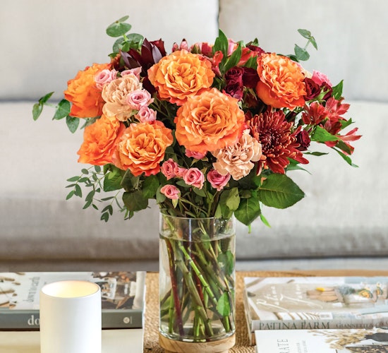 Vibrant orange and pink roses combined with lush greenery in a stylish vase.