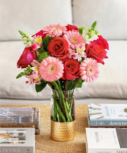Vibrant floral arrangement featuring red roses, pink gerberas, and lush greenery in a chic vase.