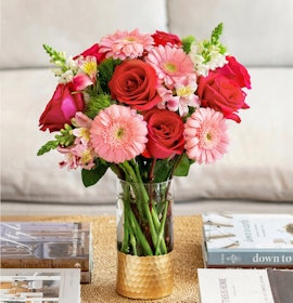 Vibrant floral arrangement of red roses and pink gerbera daisies in a chic vase.