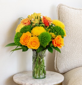Vibrant yellow and orange flower bouquet in a glass vase, perfect for brightening any room.