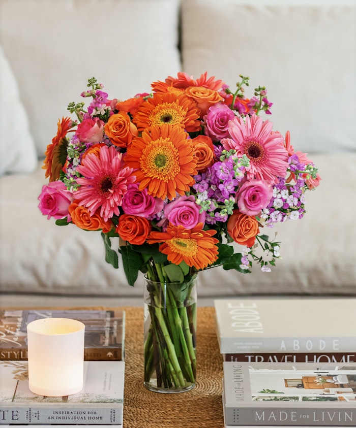 Vibrant bouquet of orange gerbera daisies and pink roses in a stylish glass vase.