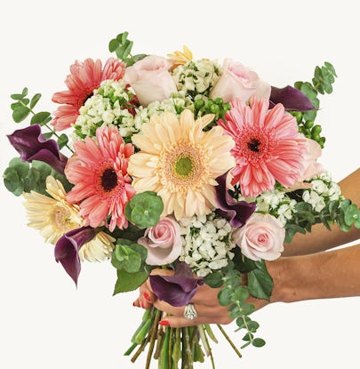 Vibrant bouquet featuring pink and peach gerbera daisies, elegant roses, and greenery.