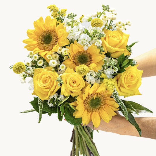 Bright and cheerful bouquet featuring sunflowers, yellow roses, and white accents.