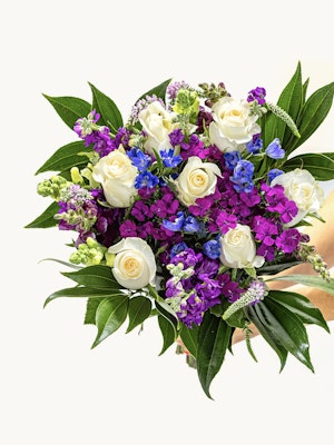 Vibrant bouquet featuring white roses, purple, and blue flowers with lush green leaves.