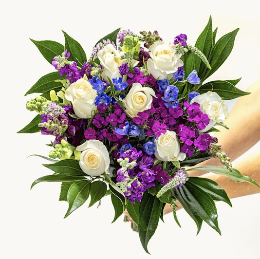 Vibrant bouquet featuring white roses, purple, and blue flowers with lush green leaves.