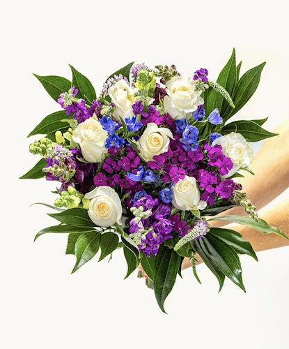 Vibrant bouquet featuring white roses, purple, and blue flowers with lush green leaves.