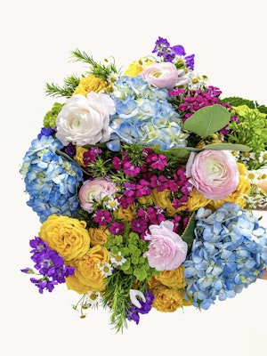 Vibrant floral bouquet featuring blue hydrangeas, pink ranunculus, and yellow roses.
