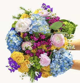 Vibrant floral bouquet featuring blue hydrangeas, pink ranunculus, and yellow roses.