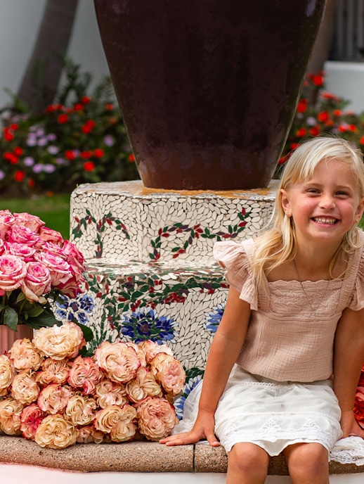 A joyful girl posing next to a colorful rose arrangement in a beautiful garden setting.