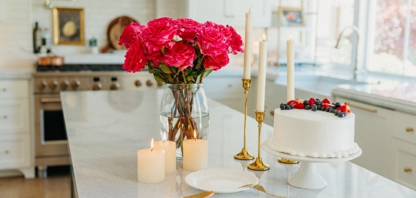 Vibrant pink roses in a vase alongside candles and a beautifully decorated cake on a modern kitchen island.