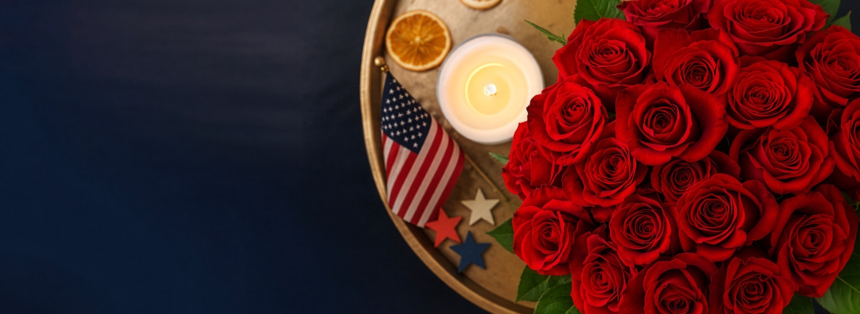 A vibrant bouquet of red roses beside a glowing candle and patriotic decor.