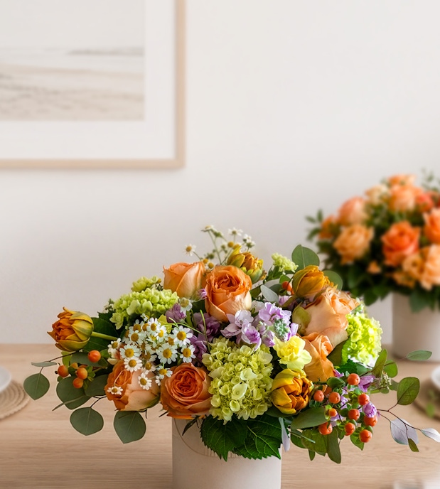 Vibrant floral arrangement featuring orange roses, daisies, and greenery in a chic vase.