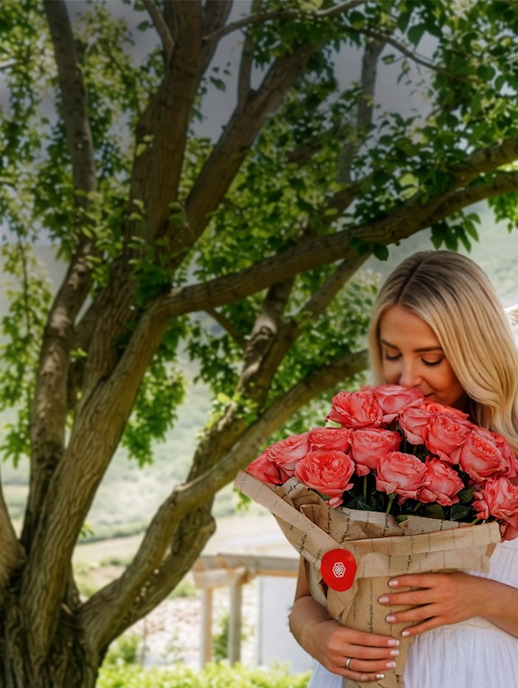 A woman in a white dress joyfully holds a large bouquet of peach roses outdoors.