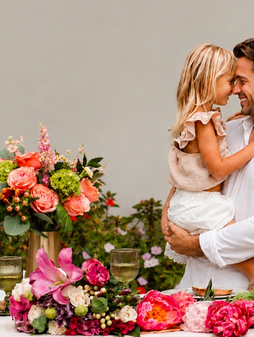 A joyful father and daughter share a sweet moment beside a vibrant floral arrangement.
