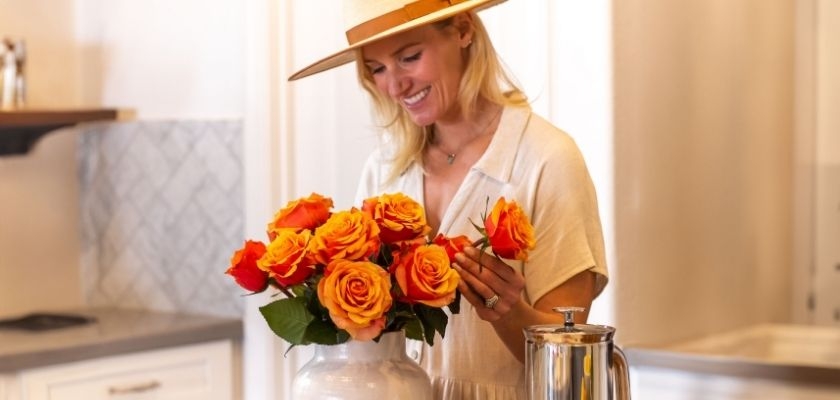 Woman arranging vibrant orange roses in a stylish kitchen, showcasing her creativity.
