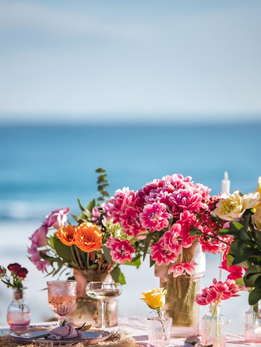 Colorful floral centerpiece with pink and orange blooms by the seaside, perfect for events.