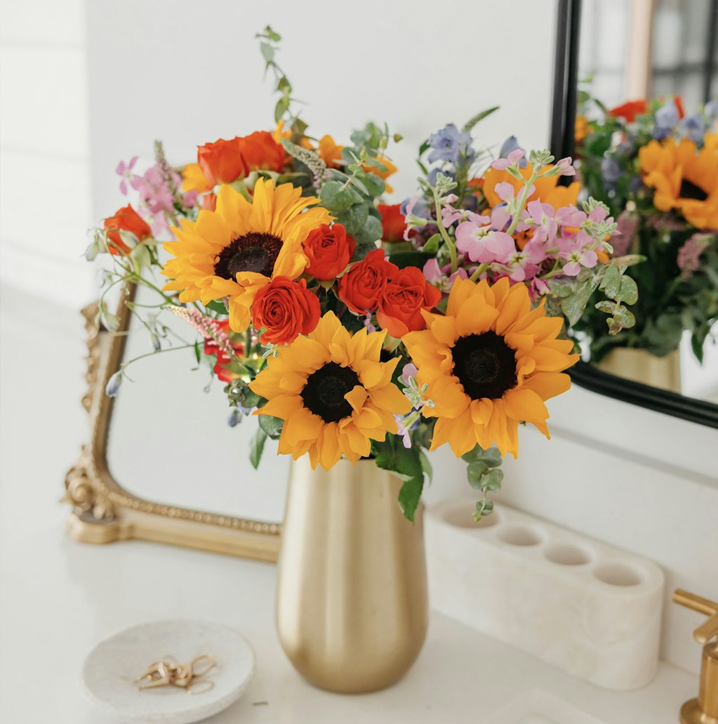 Vibrant floral arrangement featuring sunflowers, roses, and colorful blooms in a chic vase.