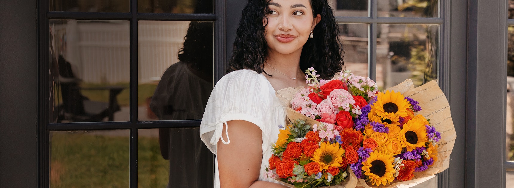 A woman stands by a door, holding vibrant bouquets of mixed flowers, ideal for celebrations.
