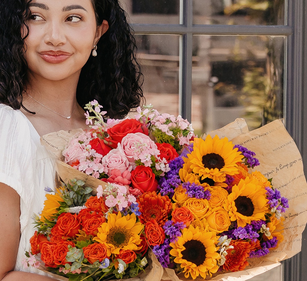 Woman holding vibrant bouquets filled with sunflowers, roses, and colorful blooms.