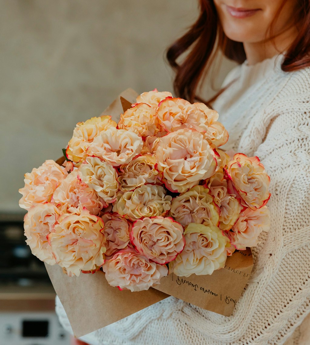 A lovely bouquet of peach and pink roses elegantly wrapped in brown paper.