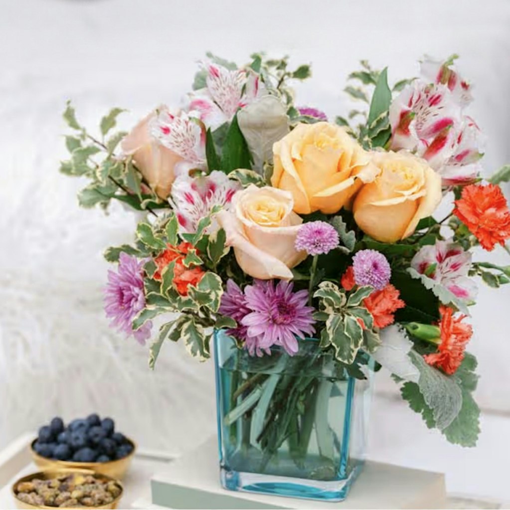 Vibrant floral arrangement featuring peach roses, colorful blooms, and lush greenery.