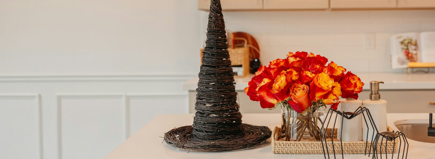 A striking centerpiece featuring a tall black witch hat and vibrant orange roses.