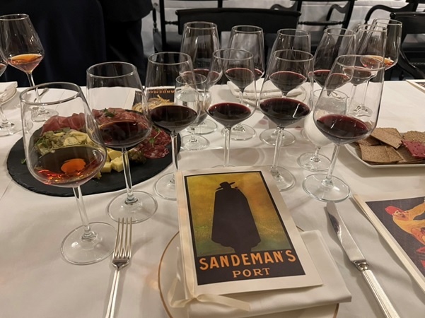 Uma mesa está posta para uma degustação com múltiplos copos de vinho, pequenos aperitivos e brochuras "Sandeman's Port"