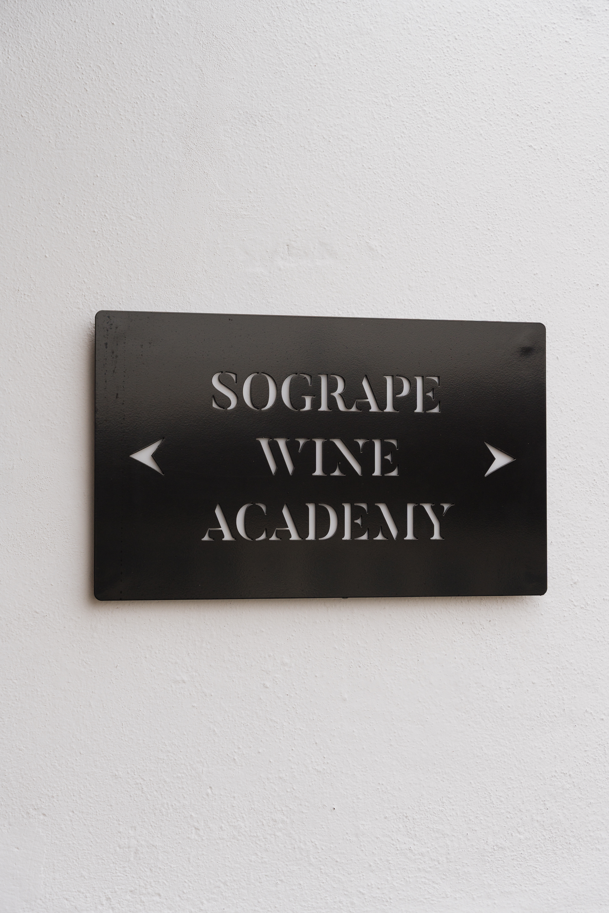 Um letreiro preto fixo numa parede branca indica a "Sogrape Wine Academy" com setas apontando para ambos os lados